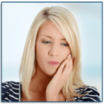 blonde woman holding the side of her jaw in need of an emergency dentist